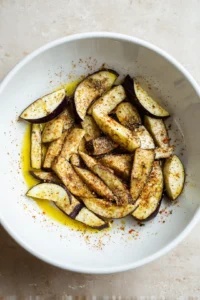 Slice the eggplant into fry-shaped pieces and place them in a bowl. Drizzle with olive oil and sprinkle with salt, garlic powder, paprika, and black pepper. Toss to coat evenly.