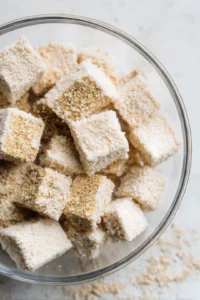 Coat the marinated tofu with panko breadcrumbs and nutritional yeast, then place in air fryer