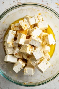 Combine cubed tofu with olive oil and sriracha sauce in a mixing bowl