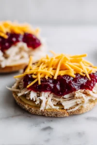 Layer shredded turkey and cheddar cheese on top of cranberry sauce, then place mustard-spread slice of bread on top to form a sandwich