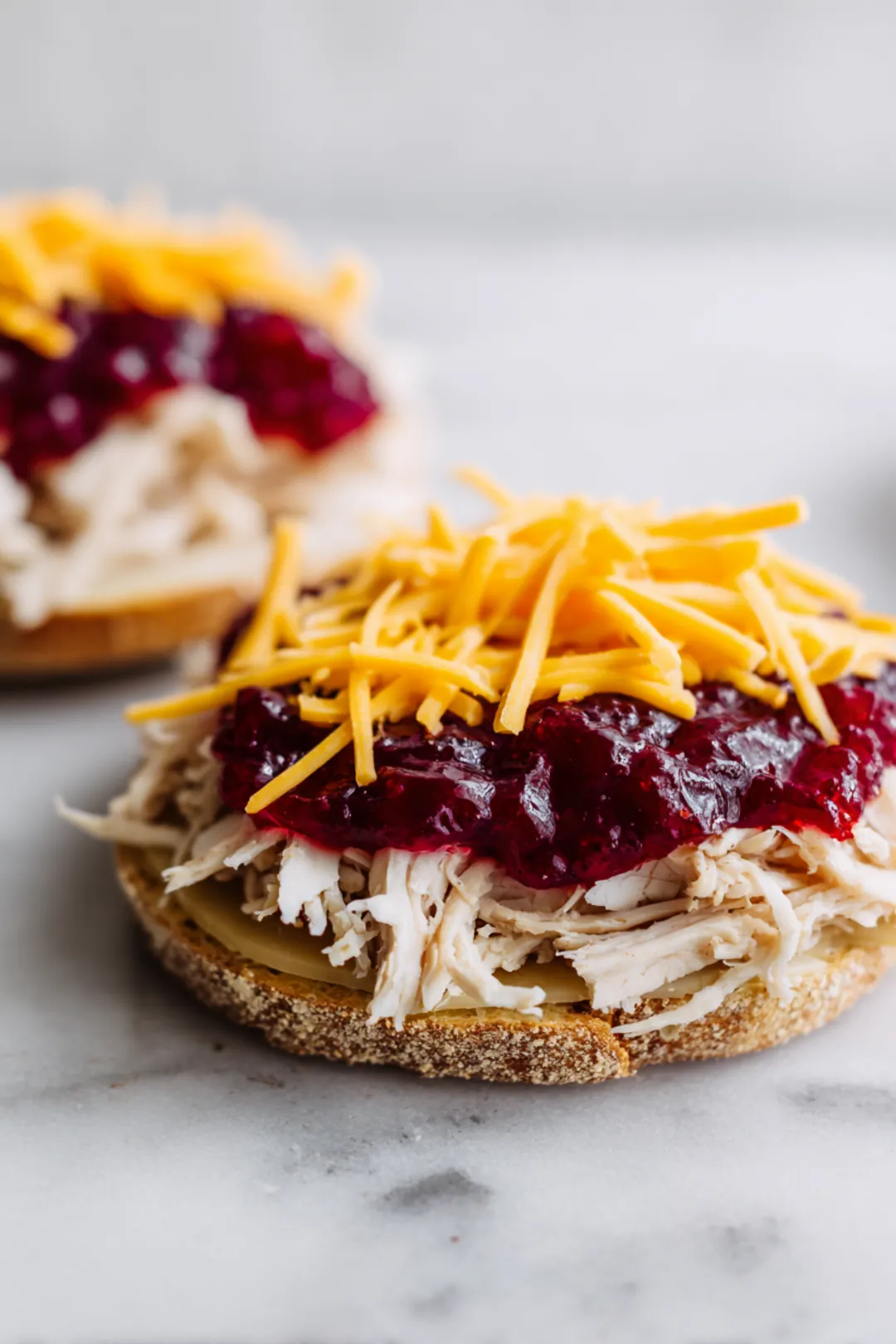 Layer shredded turkey and cheddar cheese on top of cranberry sauce, then place mustard-spread slice of bread on top to form a sandwich