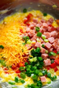 Add diced spam, bell pepper, green onions, and half of the shredded cheese to the egg mixture and stir until evenly combined