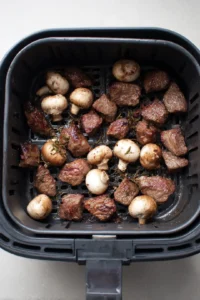 Arrange marinated steak and sliced mushrooms in the air fryer