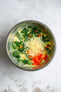 Combine chopped spinach, diced bell pepper, and shredded cheese into the egg mixture