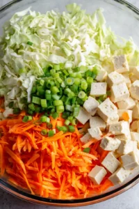 Prepare the filling by combining cabbage, carrots, tofu, and green onions