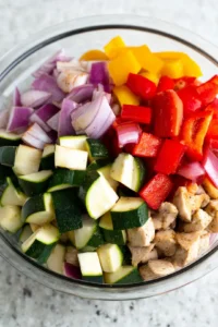 Add sliced bell pepper, onion, and zucchini to chicken mixture and cook in air fryer