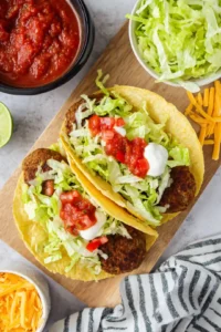 Assemble the tacos by placing a patty in each taco shell, then top with sour cream, salsa, shredded lettuce, and cheese.