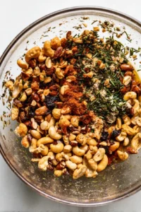 Combine mixed nuts with olive oil, chopped rosemary, salt, garlic powder, and paprika