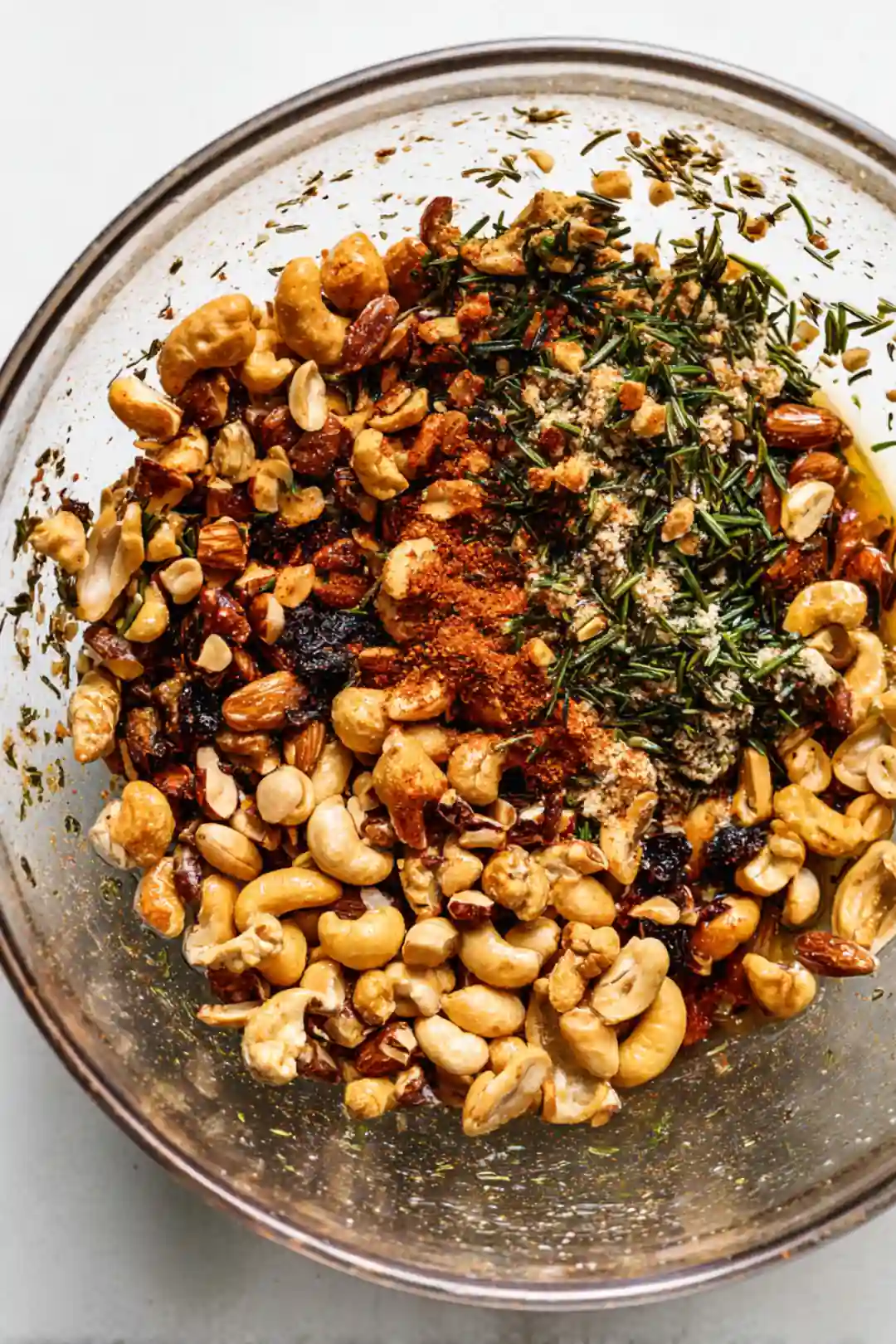 Combine mixed nuts with olive oil, chopped rosemary, salt, garlic powder, and paprika