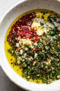Combine olive oil, red wine vinegar, minced garlic, chopped parsley, and red pepper flakes in a bowl to create the chimichurri marinade