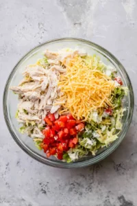 Combine shredded chicken, cheese, lettuce, and diced tomatoes in a mixing bowl