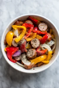 Combine sliced sausage, bell peppers, onion, olive oil, garlic powder, and Italian seasoning