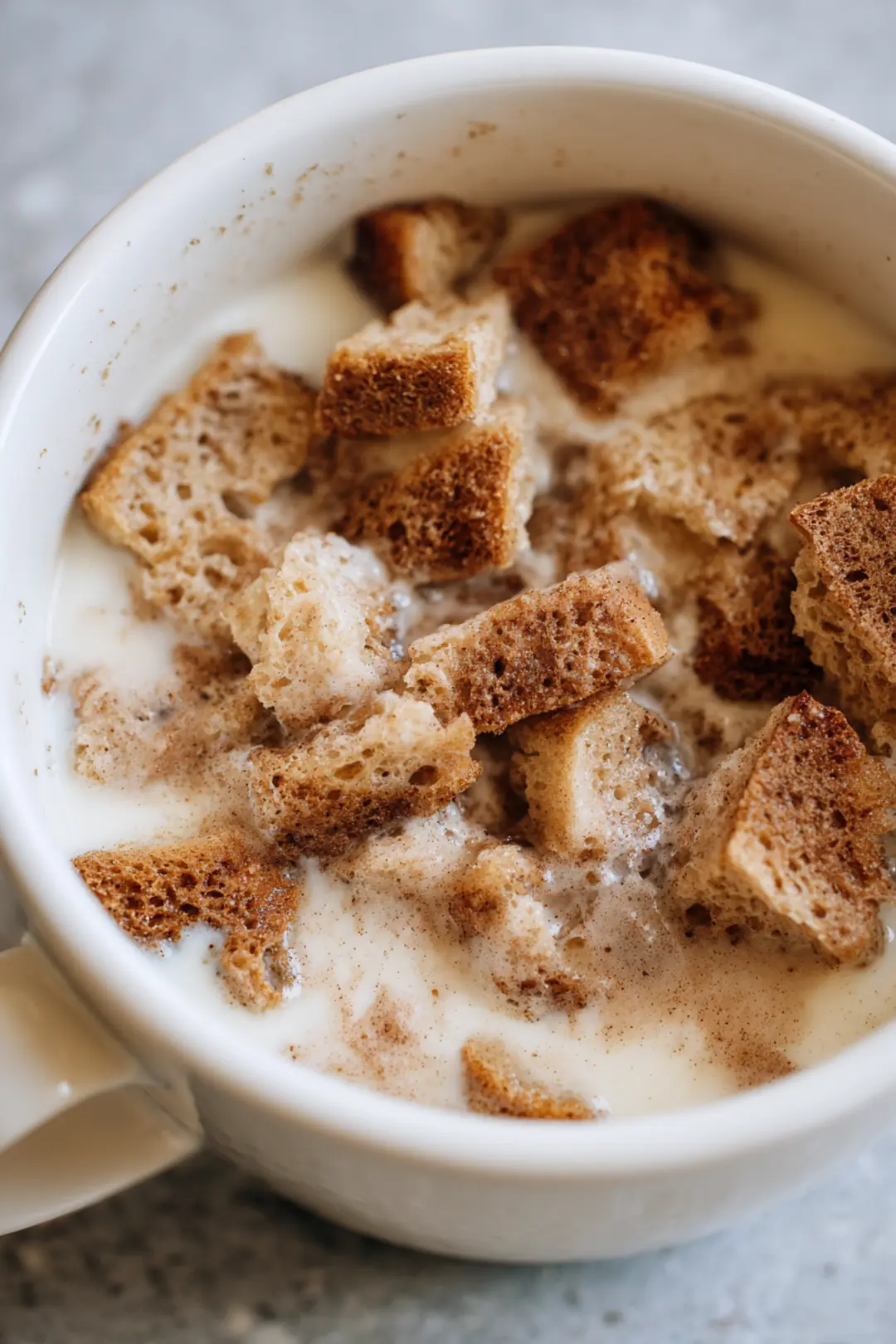 Combine torn bread pieces with egg, milk, sugar, vanilla extract, and cinnamon in a mug