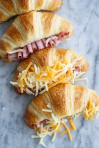 Layer the diced ham and shredded cheese between the halves and close the croissants. Place them in the air fryer basket and cook for about 10 minutes until golden and crispy.