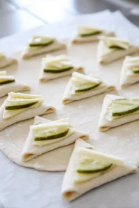 Place a pickle slice and a cheese strip on the wide end of the crescent roll triangle and roll it up tightly.