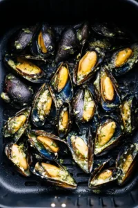 Place the cleaned mussels in a single layer in the air fryer basket and spoon garlic butter over them