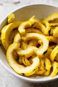 Slice delicata squash into fry shapes and toss with olive oil, salt, pepper, and garlic powder in a bowl until evenly coated