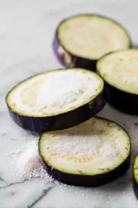 Slice the eggplant into 1/2 inch rounds and sprinkle with salt. Let them sit for about 10 minutes to draw out moisture, then pat dry with a paper towel.