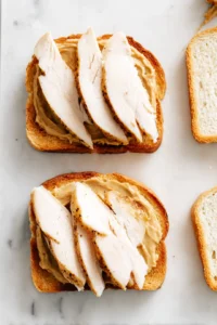 Spread a thin layer of mustard on each slice of bread and layer cooked turkey slices on top
