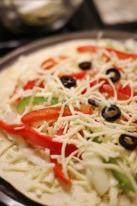 Sprinkle shredded mozzarella cheese and your chosen toppings over the sauce