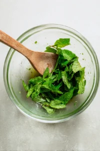 Add fresh mint leaves to the mixture and gently muddle them with a wooden spoon