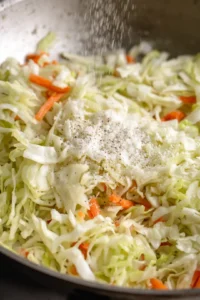 Add shredded cabbage and carrots to the pan and season with salt and black pepper