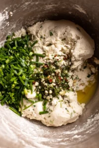 Add the sourdough discard, lukewarm water, and olive oil to the bowl, stirring until a dough forms. Incorporate the finely chopped wild garlic and pepper flakes, mixing until evenly distributed.