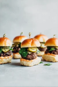 Assemble the sliders by spreading sriracha mayo on the slider buns, adding the cooked patties, pickled vegetables, and cilantro leaves. Serve immediately.