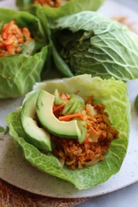 Assemble the wraps by placing the filling on a cabbage leaf and topping with avocado slices, then fold and roll tightly.