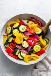 Combine bell peppers, zucchini, yellow squash, and red onion with olive oil, salt, and pepper