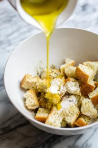 Drizzle olive oil over the bread pieces and sprinkle with salt, garlic powder, and paprika for flavor.