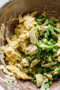 Fold in the chopped asparagus and artichoke hearts until evenly distributed throughout the batter.