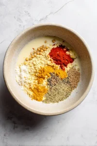 Mix together chickpea flour, water, cumin seeds, coriander powder, turmeric, red chili powder, and salt to form a thick batter