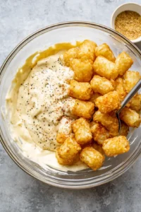 Mix together the mayonnaise, mustard, salt, and black pepper with cooled potatoes and crispy tater tots