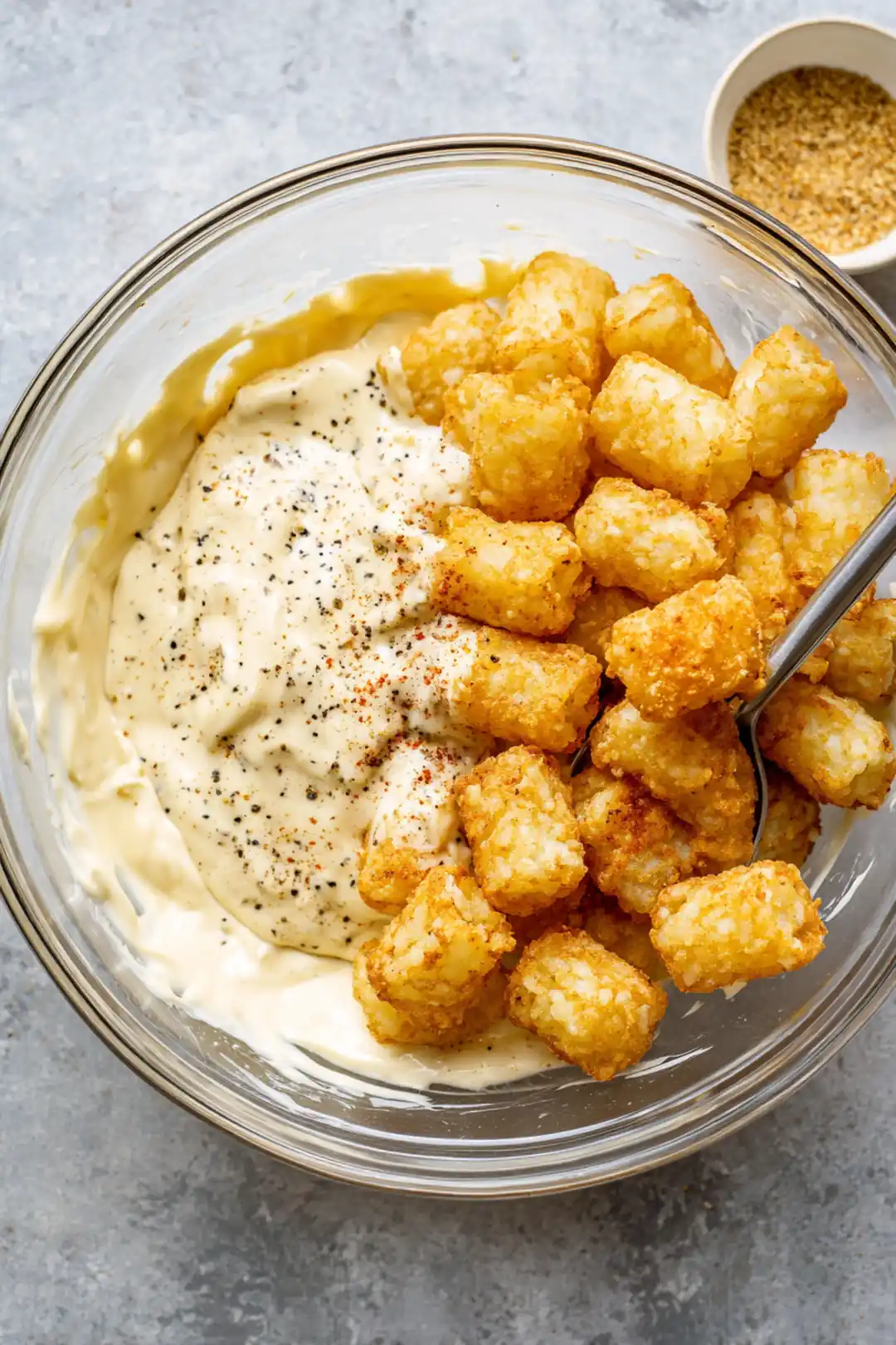 Mix together the mayonnaise, mustard, salt, and black pepper with cooled potatoes and crispy tater tots