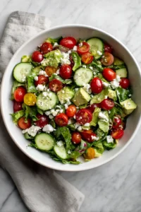 Prepare the salad with mixed greens, cherry tomatoes, cucumber, avocado, and feta cheese