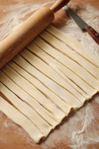 Roll out the puff pastry and cut it into strips, then arrange apple slices along the edge, fold over, and roll to create rose shape, place in air fryer and cook for 15 minutes until golden.