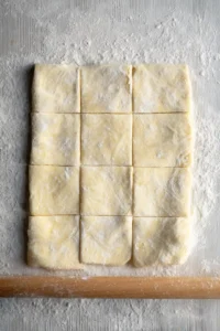 Roll out the thawed puff pastry on a lightly floured surface and cut it into squares.