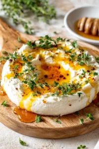 Transfer the whipped feta to a serving board and create a shallow well in the center. Drizzle hot honey over the top and sprinkle with fresh herbs.