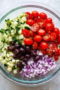 Add cherry tomatoes, cucumber, red onion, and black olives to the bowl