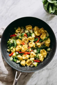 Combine cooked tortellini with basil, salt, and black pepper in the skillet
