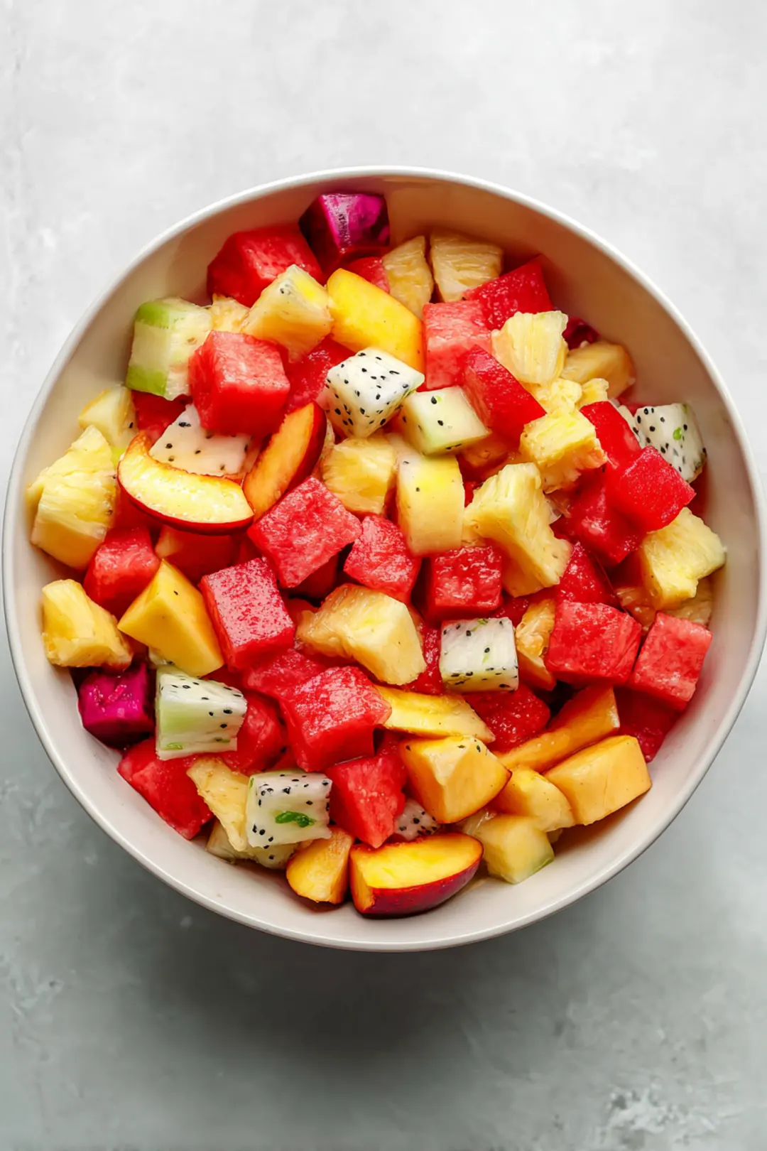 Combine diced fresh peaches, watermelon, pineapple, and dragon fruit in a large mixing bowl