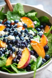 Combine fresh spinach, blueberries, sliced peaches, and crumbled feta cheese in a large bowl