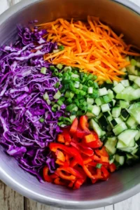 Combine shredded purple cabbage, carrots, cucumbers, red bell pepper, and green onions in a large bowl
