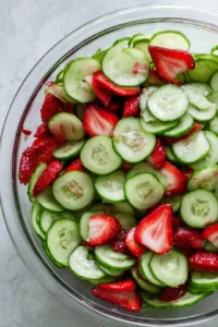 Combine sliced cucumbers and strawberries in a large bowl