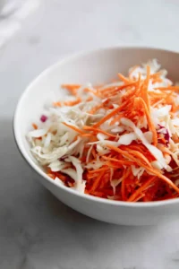 Prepare the slaw by mixing shredded cabbage, carrot, and rice vinegar