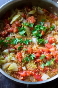 Stir in diced tomatoes, chopped cabbage, and rinsed quinoa, bring to a boil, then simmer for 25 minutes until cooked.